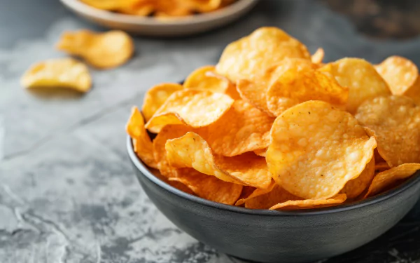 A close-up view of golden crispy potato chips in a black bowl, with a textured gray background, creating an inviting and appetizing HD desktop wallpaper.