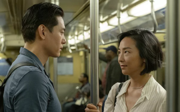 HD wallpaper featuring a scene from the movie Past Lives with two characters facing each other in a subway car.