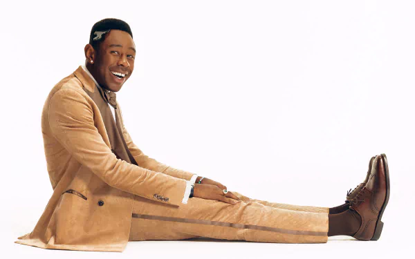 HD desktop wallpaper featuring a smiling man in a stylish beige suit, embodying the music and spirit of rapper Tyler, the Creator, against a white background.