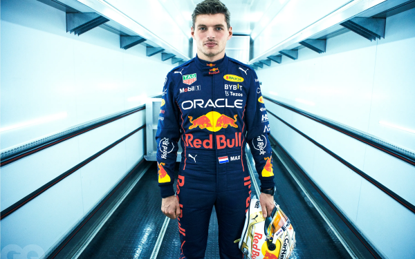 HD wallpaper of an F1 racer in full gear standing confidently in a futuristic corridor, representing the speed and precision of elite motorsports.