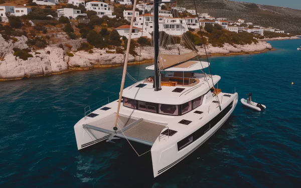 A sleek catamaran anchored near a picturesque shoreline, complemented by charming white houses on the hills above. This stunning image serves as an HD desktop wallpaper or background.