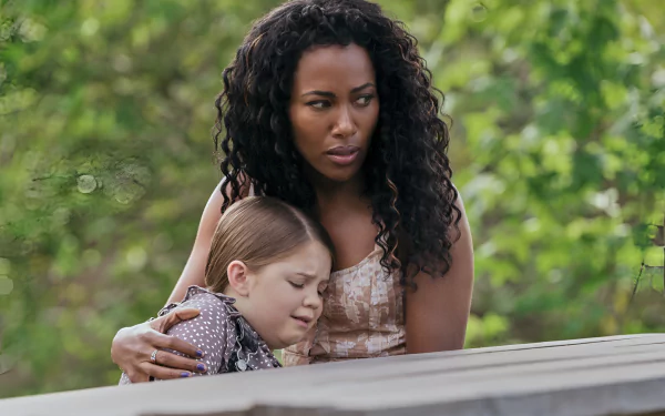A woman embraces a young girl, both expressing concern, against a backdrop of lush greenery. This evocative scene is from the movie Imaginary (2024) and makes a striking HD desktop wallpaper.