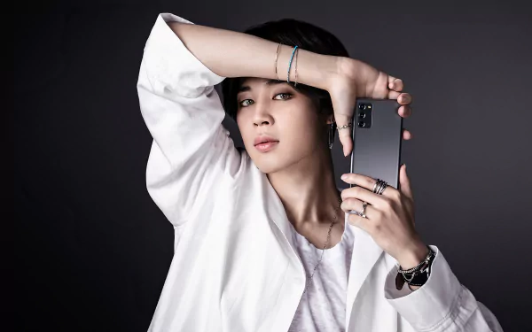 Stylish HD desktop wallpaper featuring a music artist posing artistically with a smartphone, perfect for BTS and Jimin fans.