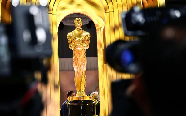 Oscar statuette in sharp focus with a golden blurred background and camera silhouette – HD Academy Awards themed desktop wallpaper.