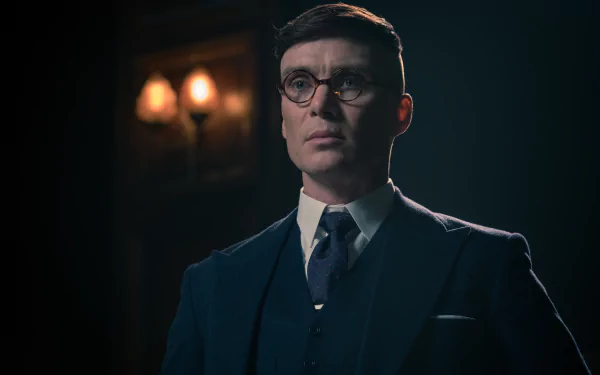 HD wallpaper featuring a dramatic portrait of the character Thomas Shelby from the TV show Peaky Blinders, showcasing a stylish suit and iconic haircut in a moody, dimly lit setting.