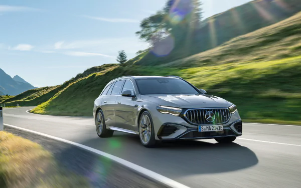 HD desktop wallpaper featuring a Mercedes-AMG E53 Hybrid car in motion on a scenic road with lush greenery in the background.