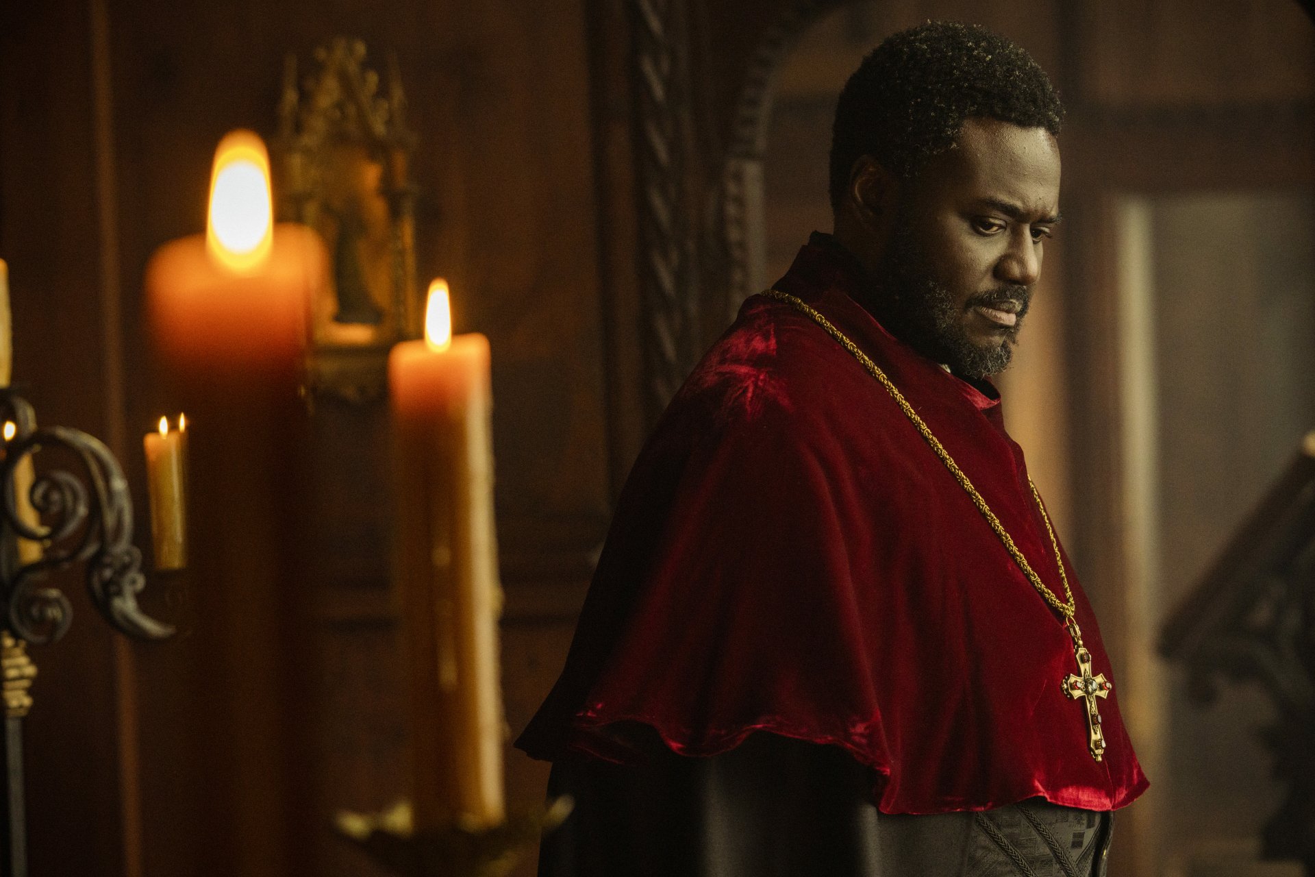 A captivating HD desktop wallpaper from the TV show Shardlake, featuring a character in a red robe with a cross, illuminated by candlelight in a dramatic, historical setting.