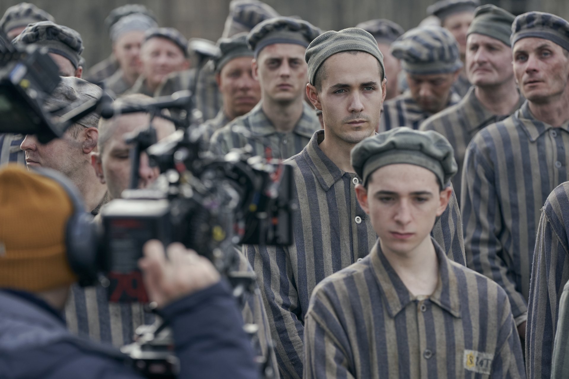 HD desktop wallpaper of a scene from The Tattooist of Auschwitz TV show, depicting actors in prisoner uniforms during filming.