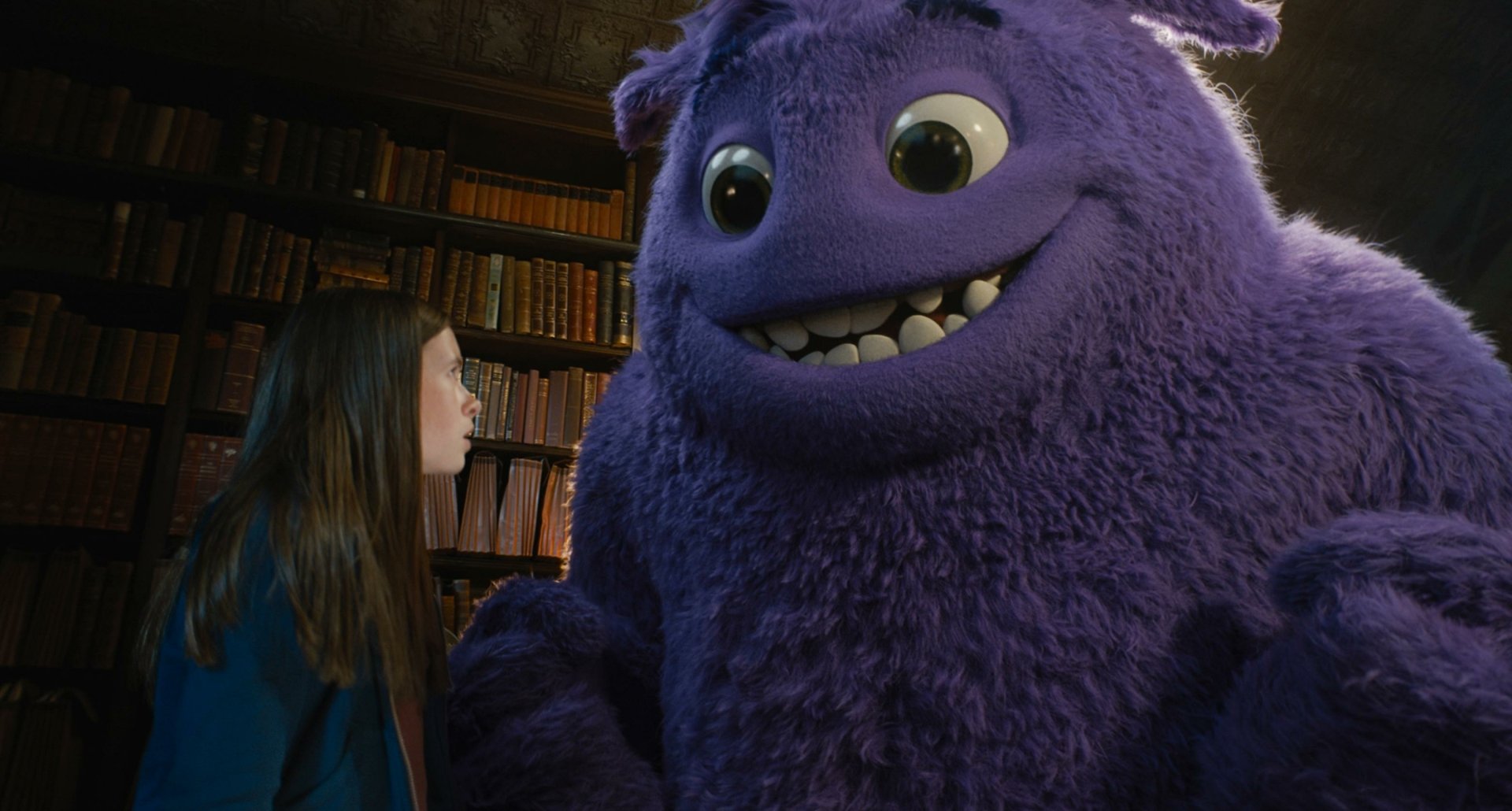 A scene from the movie IF (2024) featuring Cailey Fleming with a large purple furry creature, set in an environment filled with books. This HD desktop wallpaper showcases the enchanting interaction.