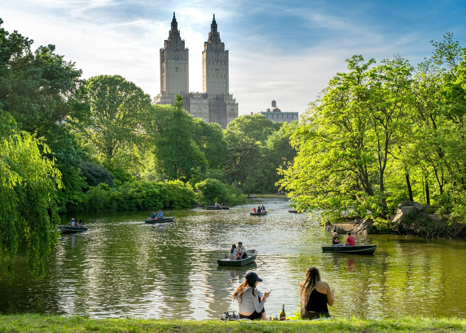 HD desktop wallpaper featuring Central Park in New York, showcasing a picturesque lake with several boats and lush greenery, framed by iconic city buildings in the background.