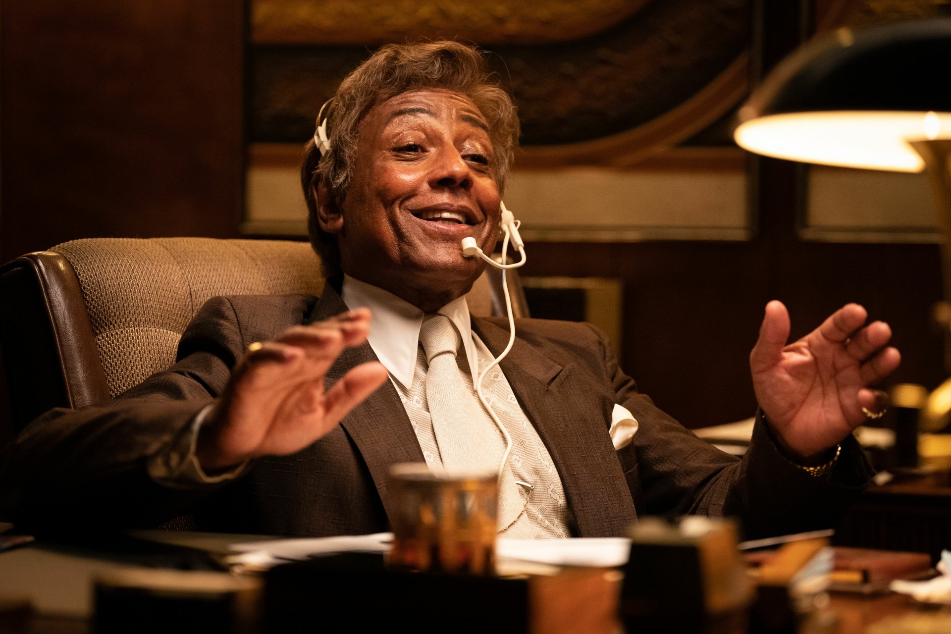 HD desktop wallpaper featuring Giancarlo Esposito in the movie Maxxxine, seated at a desk with a headset, exuding confidence and charisma.
