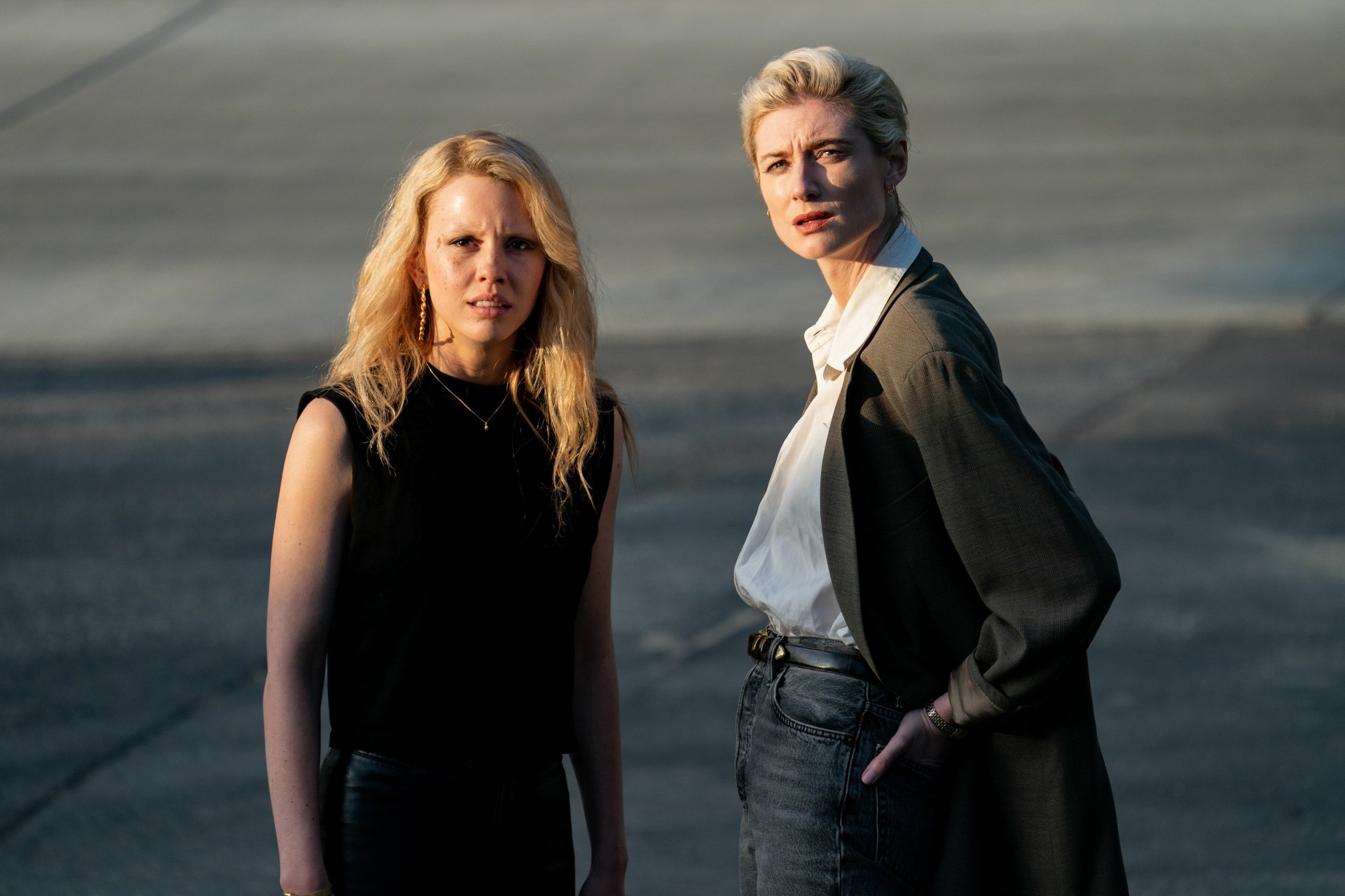 HD desktop wallpaper of movie Maxxxine featuring Mia Goth and Elizabeth Debicki. They stand outdoors, bathed in soft sunlight, projecting intense expressions.
