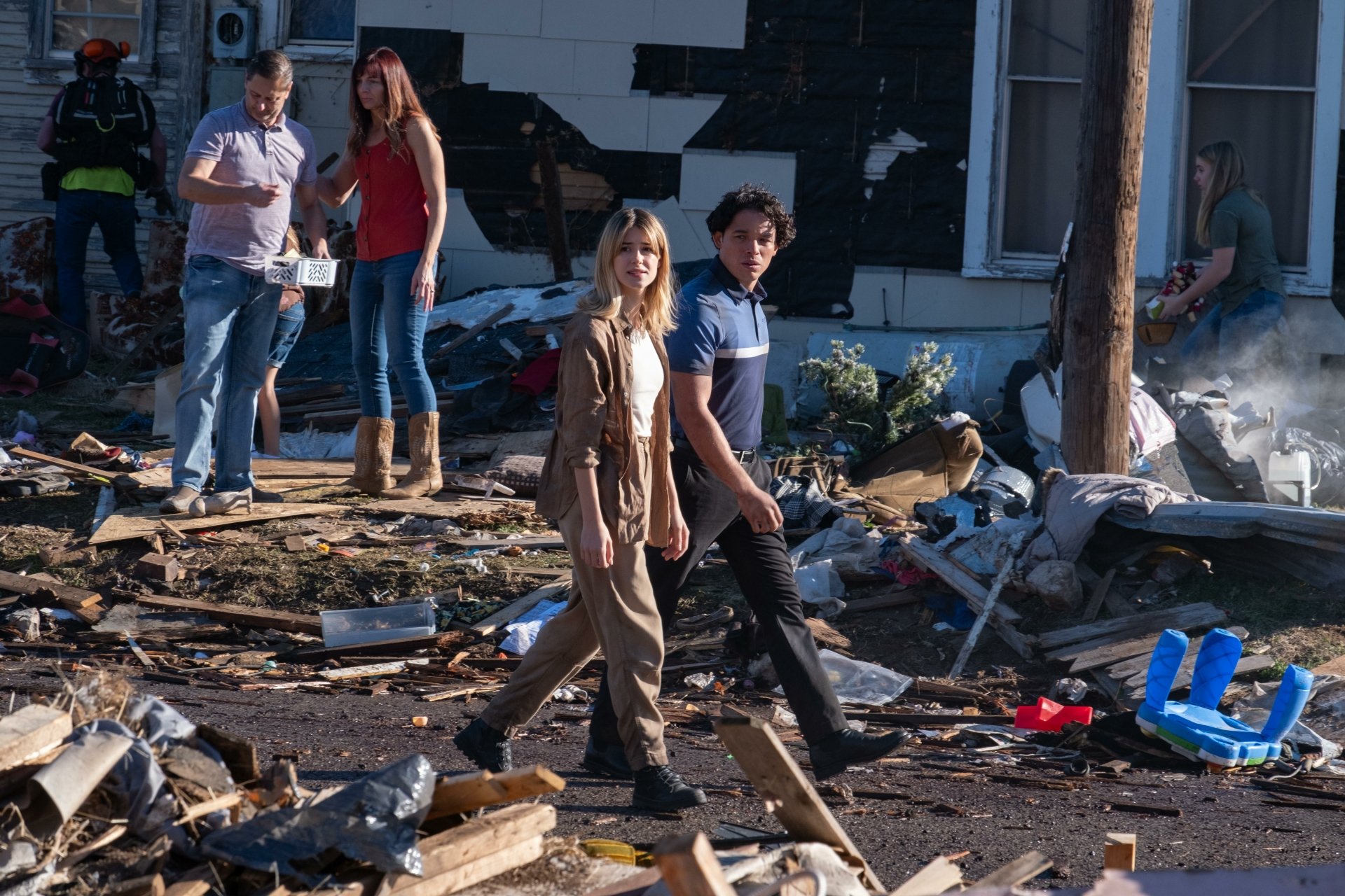 Two people walk through a debris-strewn area with others in the background, from the movie Twisters. This HD desktop wallpaper and background conveys a sense of chaos and aftermath.