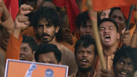 HD desktop wallpaper from the movie Monkey Man (2024), featuring a focused man amidst an exuberant crowd at a rally.
