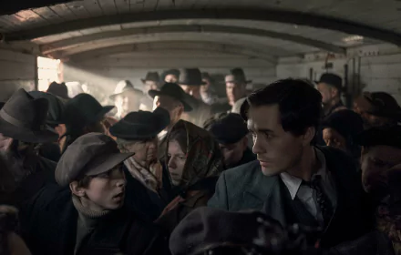 HD desktop wallpaper from the TV show The Tattooist of Auschwitz, depicting a crowded scene with a thoughtful young man looking ahead.