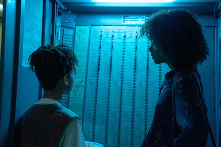 HD desktop wallpaper from the movie I Saw the TV Glow, featuring two characters in a blue-lit room facing a curtain-covered window.