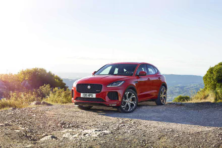 HD wallpaper of a red Jaguar E-Pace parked on a gravel road with scenic hills and greenery in the background.