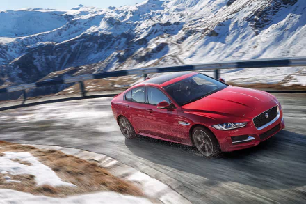 HD desktop wallpaper featuring a Jaguar XE AWD in vibrant red, driving through a snowy mountainous landscape.