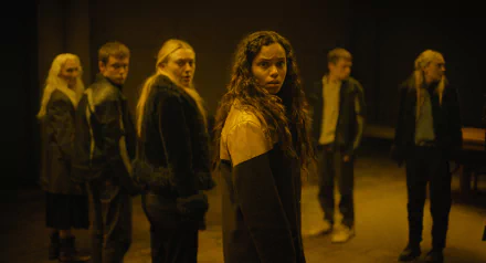 A tense scene from the movie The Watchers (2024), featuring Georgina Campbell amidst a group of people in a dimly lit setting. HD desktop wallpaper and background image.