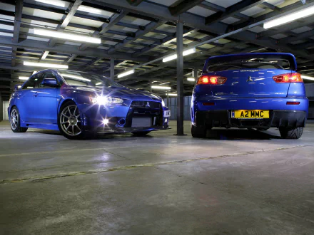 HD desktop wallpaper featuring two Mitsubishi Lancer Evolution X cars in a garage, showcasing both front and rear views.