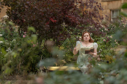 A scene from the TV show Bridgerton features a woman in a light green dress, walking through a lush garden filled with vibrant flowers and greenery, creating a captivating wallpaper backdrop.