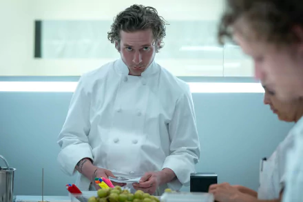HD wallpaper of Jeremy Allen White from the TV show The Bear, featuring him in a chef's uniform focused on a task in a professional kitchen setting.