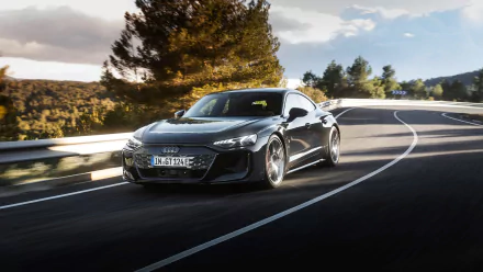 HD desktop wallpaper of an Audi RS e-Tron GT driving on a scenic road surrounded by trees and a clear sky.