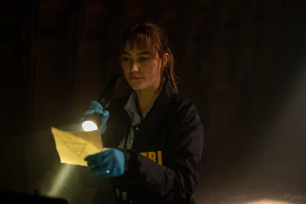 A scene from the movie Longlegs shows an investigator examining a piece of evidence with a flashlight in a dimly lit room. This HD wallpaper serves as a captivating background for desktops.