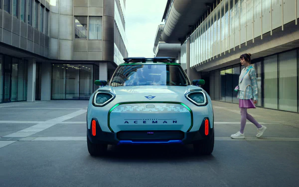 HD wallpaper featuring a MINI Aceman car in an urban setting, with a person walking by.