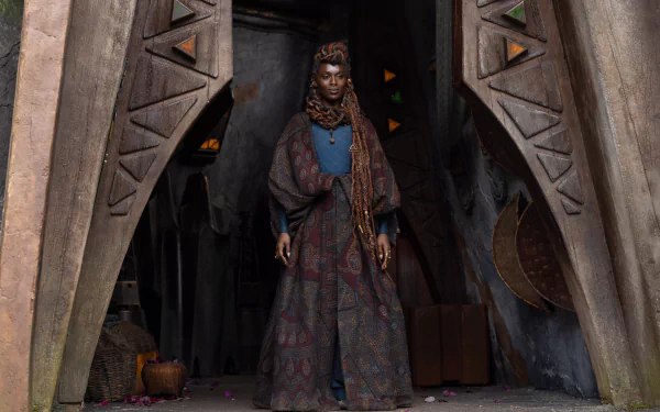 A character from the TV show The Acolyte (2024) stands in an ornate doorway, clad in intricate, robe-like attire. This HD desktop wallpaper captures a mystical and immersive scene from the series.