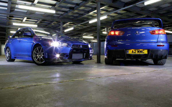 HD desktop wallpaper featuring two Mitsubishi Lancer Evolution X cars in a garage, showcasing both front and rear views.
