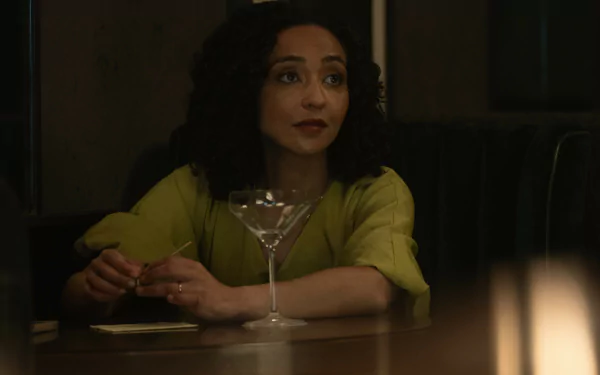 HD desktop wallpaper featuring Ruth Negga from the 2024 TV show Presumed Innocent. Ruth sits at a dim-lit bar with a cocktail glass in front of her, wearing a green blouse and an expression of contemplation.