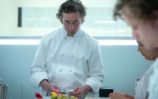 HD wallpaper of Jeremy Allen White from the TV show The Bear, featuring him in a chef's uniform focused on a task in a professional kitchen setting.