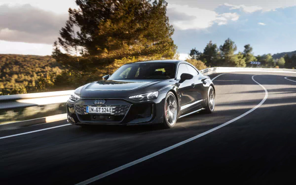 HD desktop wallpaper of an Audi RS e-Tron GT driving on a scenic road surrounded by trees and a clear sky.