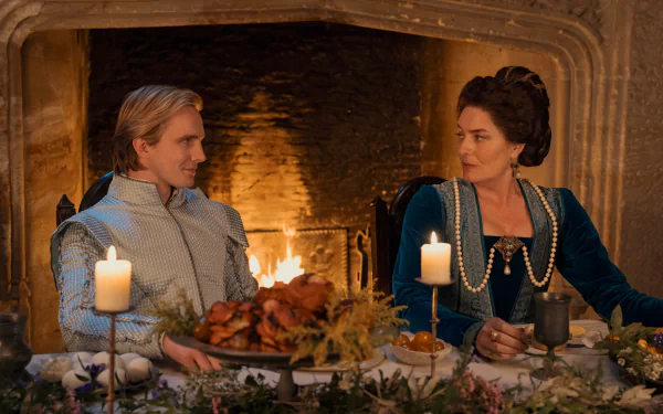 A scene from the movie My Lady Jane featuring two characters in period costumes, sitting at a decorated dinner table with candles, in front of a lit fireplace. HD desktop wallpaper and background.