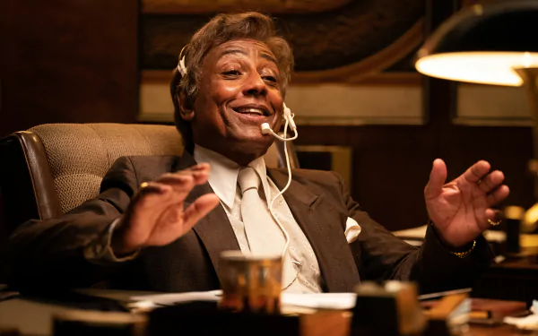 HD desktop wallpaper featuring Giancarlo Esposito in the movie Maxxxine, seated at a desk with a headset, exuding confidence and charisma.