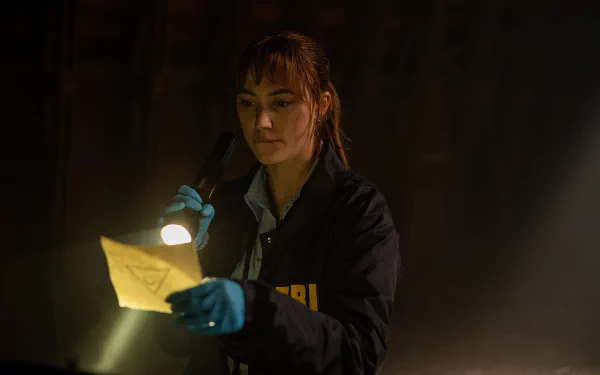A scene from the movie Longlegs shows an investigator examining a piece of evidence with a flashlight in a dimly lit room. This HD wallpaper serves as a captivating background for desktops.