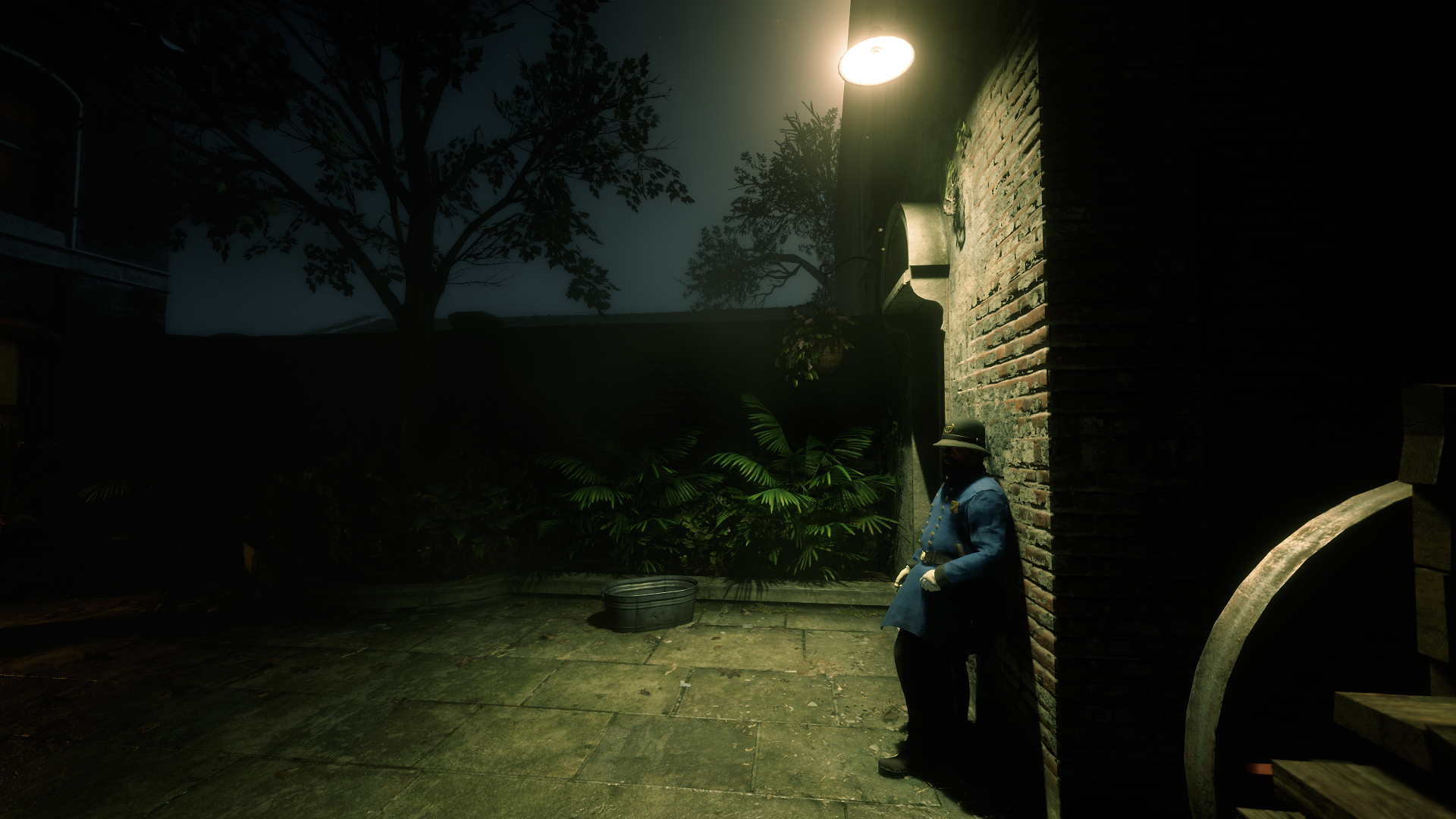 Dark, moody courtyard scene from Red Dead Redemption 2, featuring a lone character seated against a brick wall under a streetlamp, rendered as a HD PC desktop wallpaper.