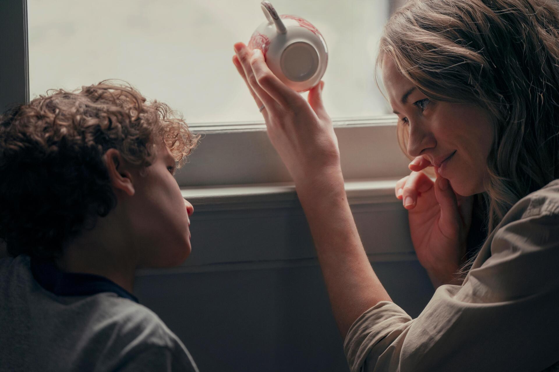 A touching moment between a woman and a child, discussing a teacup by the window, captured in stunning detail. From the TV show Teacup (2024), this 4K Ultra HD wallpaper highlights their bond.