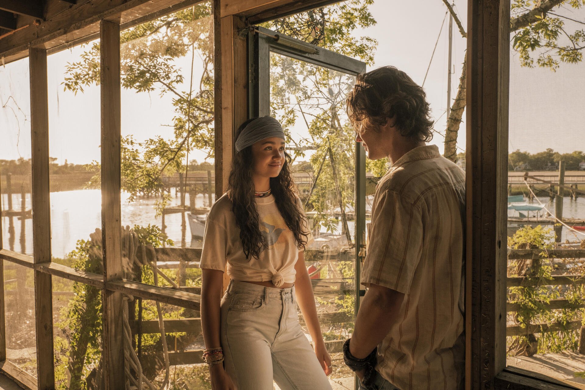 A serene moment from the TV show Outer Banks featuring Madison Bailey and Chase Stokes, set against a backdrop of sunlight and natural scenery.
