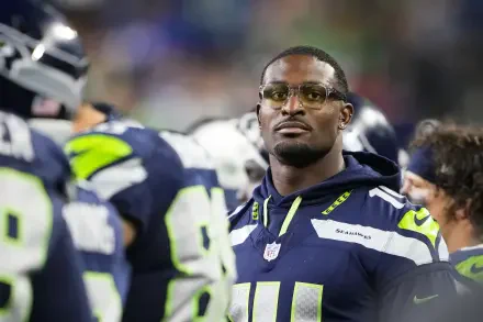 A focused DK Metcalf stands on the sidelines during an NFL game, wearing a Seattle Seahawks jersey. This high-definition image captures the intensity of the sport.