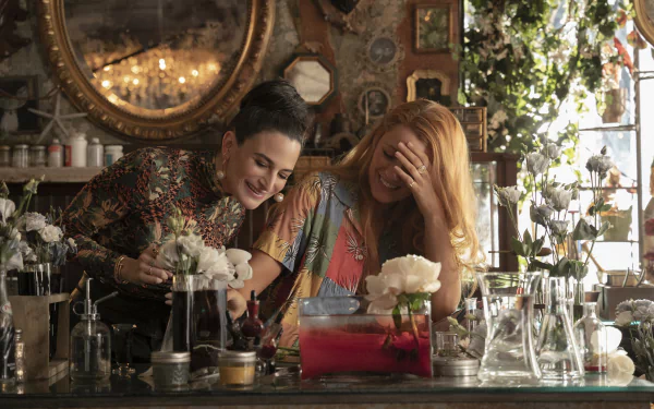 A vibrant scene from the movie It Ends with Us, featuring Blake Lively and Jenny Slate enjoying a lighthearted moment in a floral-filled setting, captured in stunning HD quality.