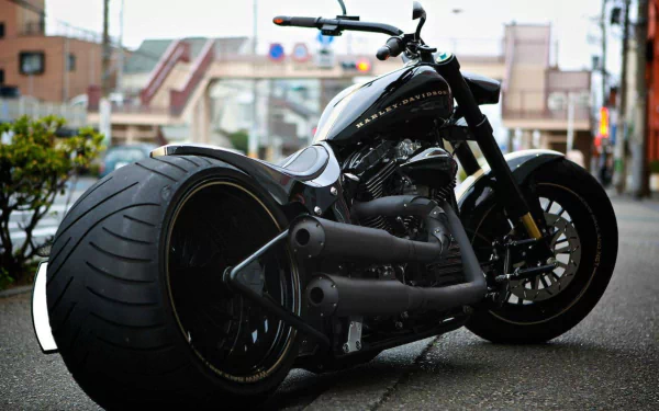 A striking Harley-Davidson chopper stands prominently on a city street, showcasing its sleek design and large rear tire, captured beautifully for a high-definition desktop wallpaper.