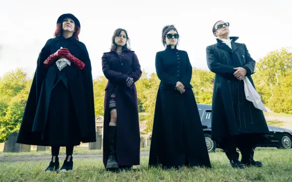 A group of four characters in dark, stylish outfits stands confidently outdoors, evoking the quirky aesthetic of Beetlejuice. This image serves as an 8K Ultra HD PC desktop wallpaper and background.