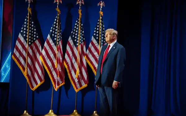 HD desktop wallpaper featuring Donald Trump standing in front of multiple American flags with a dark blue backdrop, reflecting the MAGA theme.