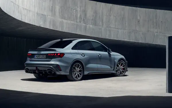 A sleek Audi RS3 Sedan parked in a modern architectural setting, showcasing its dynamic design and performance features in stunning 4K Ultra HD clarity.