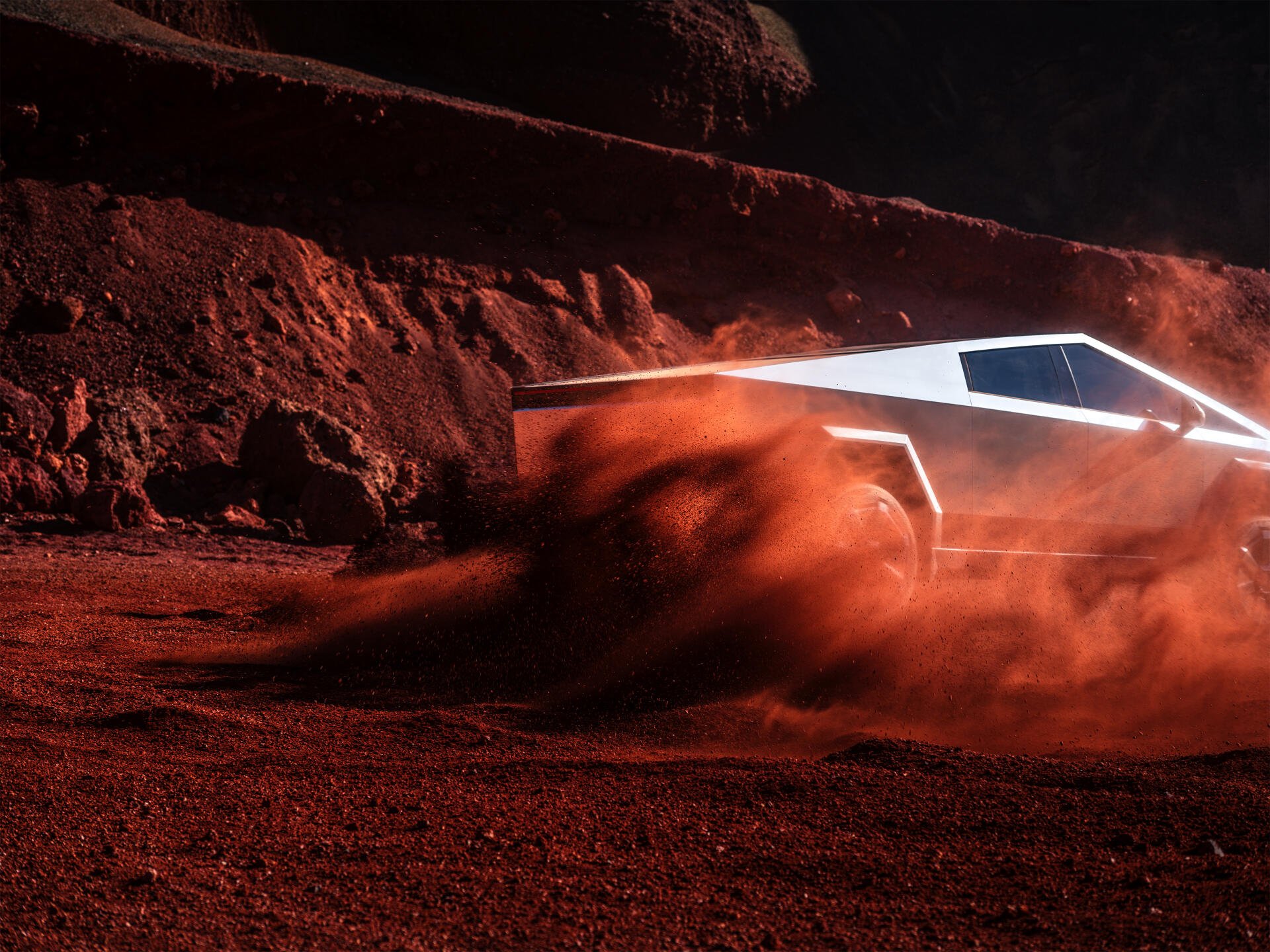 Tesla Cybertruck kicks up red dust as it drives across a rugged Martian-like terrain. 4K Ultra HD PC desktop wallpaper showcasing the futuristic electric vehicle.