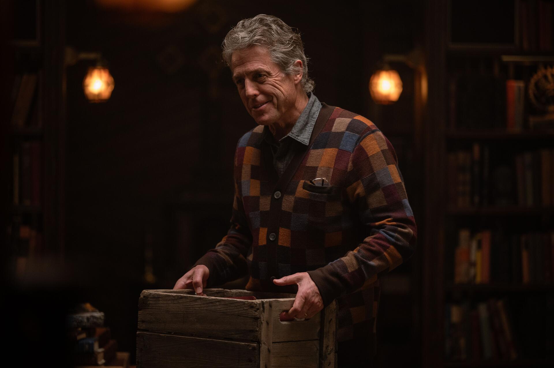 A scene from the movie Heretic (2024) featuring Hugh Grant, showcasing a warm, atmospheric setting with dim lighting and a wooden crate. 4K Ultra HD wallpaper.