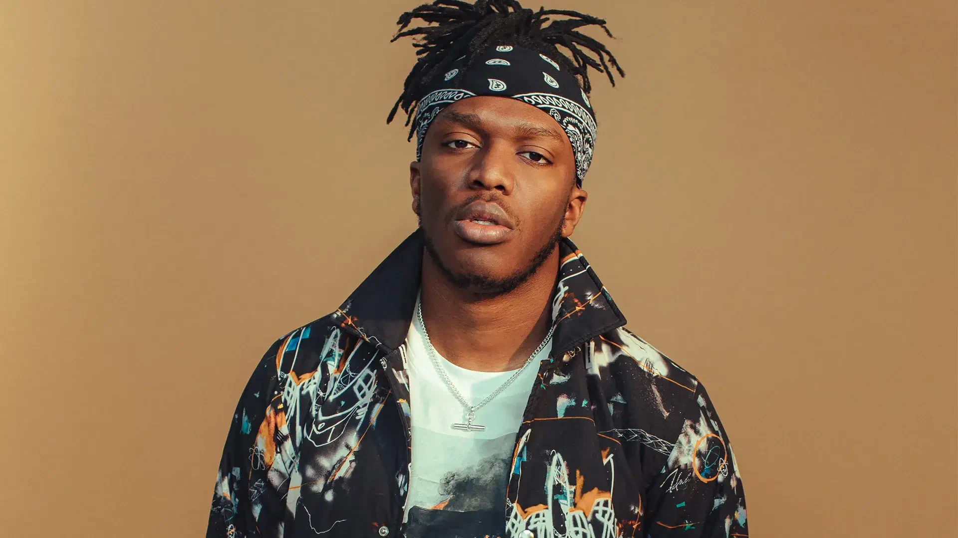 High-definition desktop wallpaper featuring KSI, showcasing him in a stylish outfit with a bandana against a warm beige background.