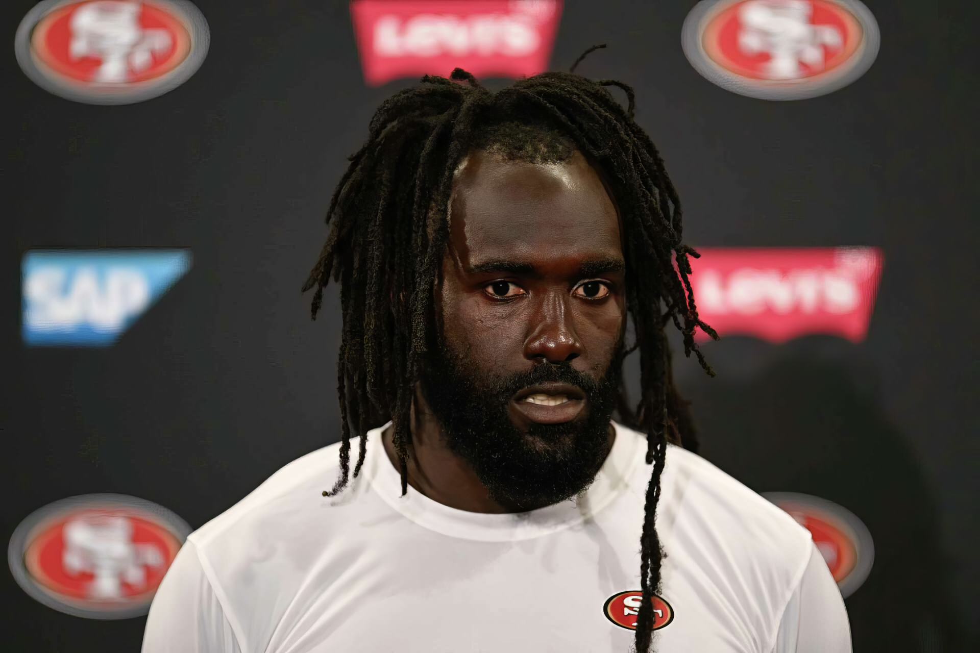 De'Vondre Campbell speaks during a San Francisco 49ers press conference, showcasing team spirit with the logo in the background. HD wallpaper capturing the intensity of football.